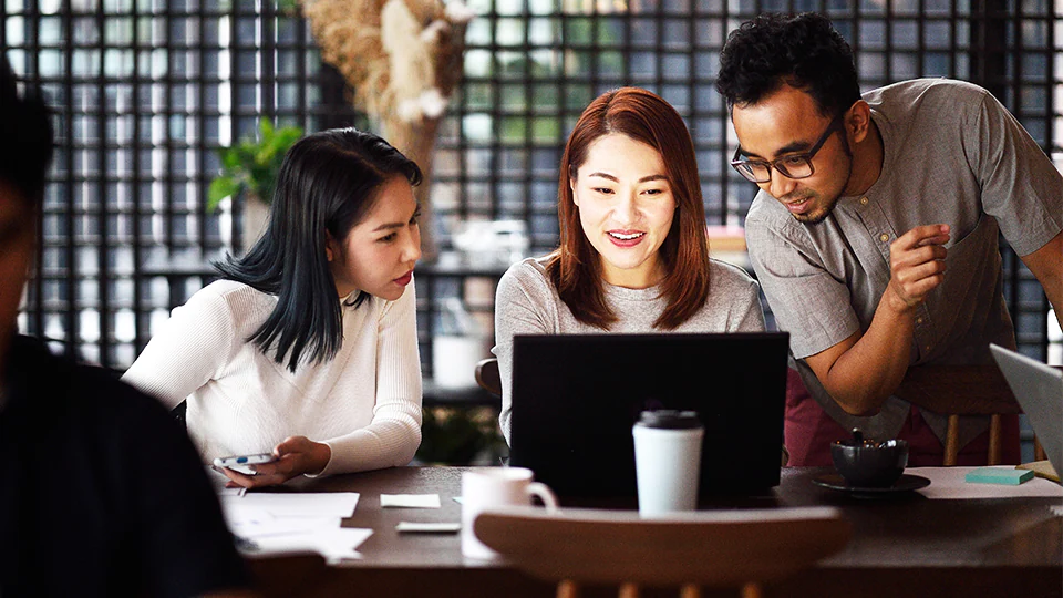 Group of people collaborating together while looking at a laptop