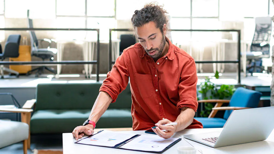 Businessman standing at desk, with laptop open paying bills.